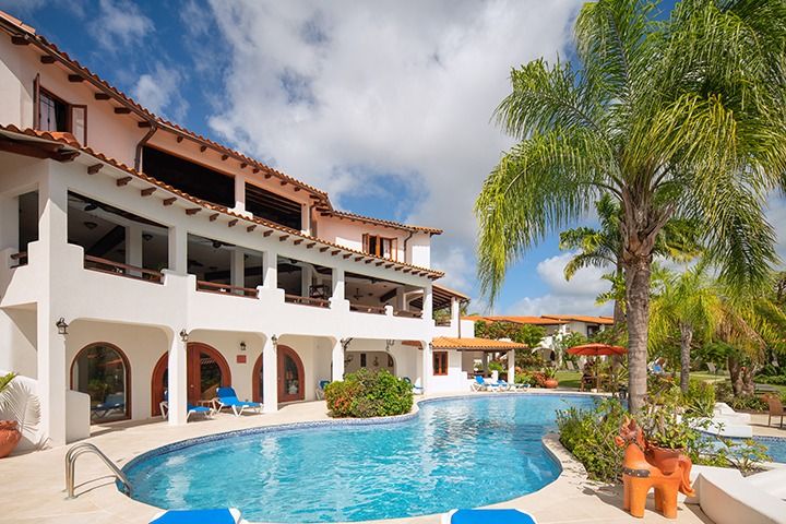 A luxurious resort pool with a palm tree and multi-story white building under a blue sky.